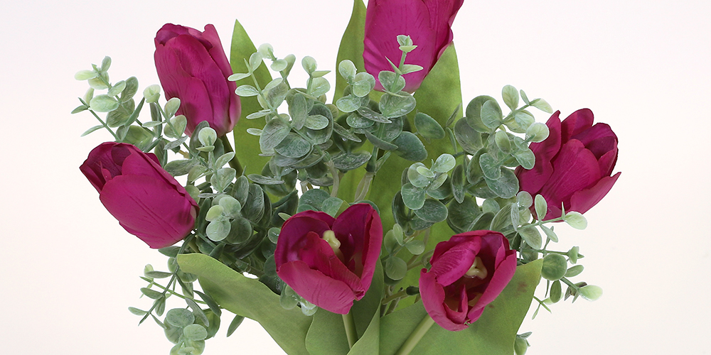 En närbild på en bukett med konstgjorda lila tulpaner och gröna blad, blandade med små gröna kvistar av eukalyptusliknande blad.