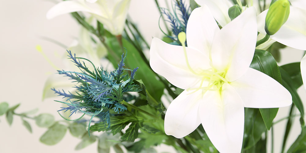 En bukett med konstgjorda vita liljor och blå blommor som omfamnas av massor av gröna blad.